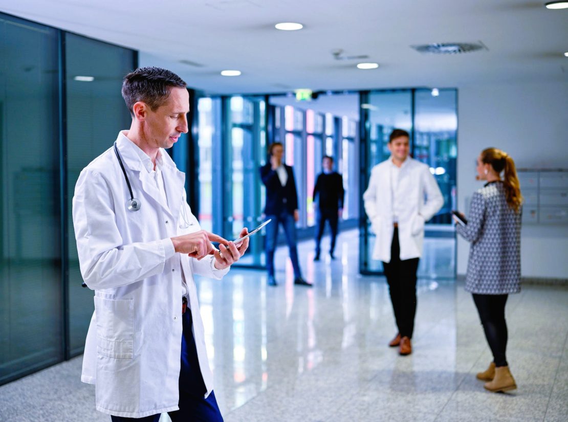 Arzt scrollt am Tablet in der Eingangshalle eines Krankenhauses.